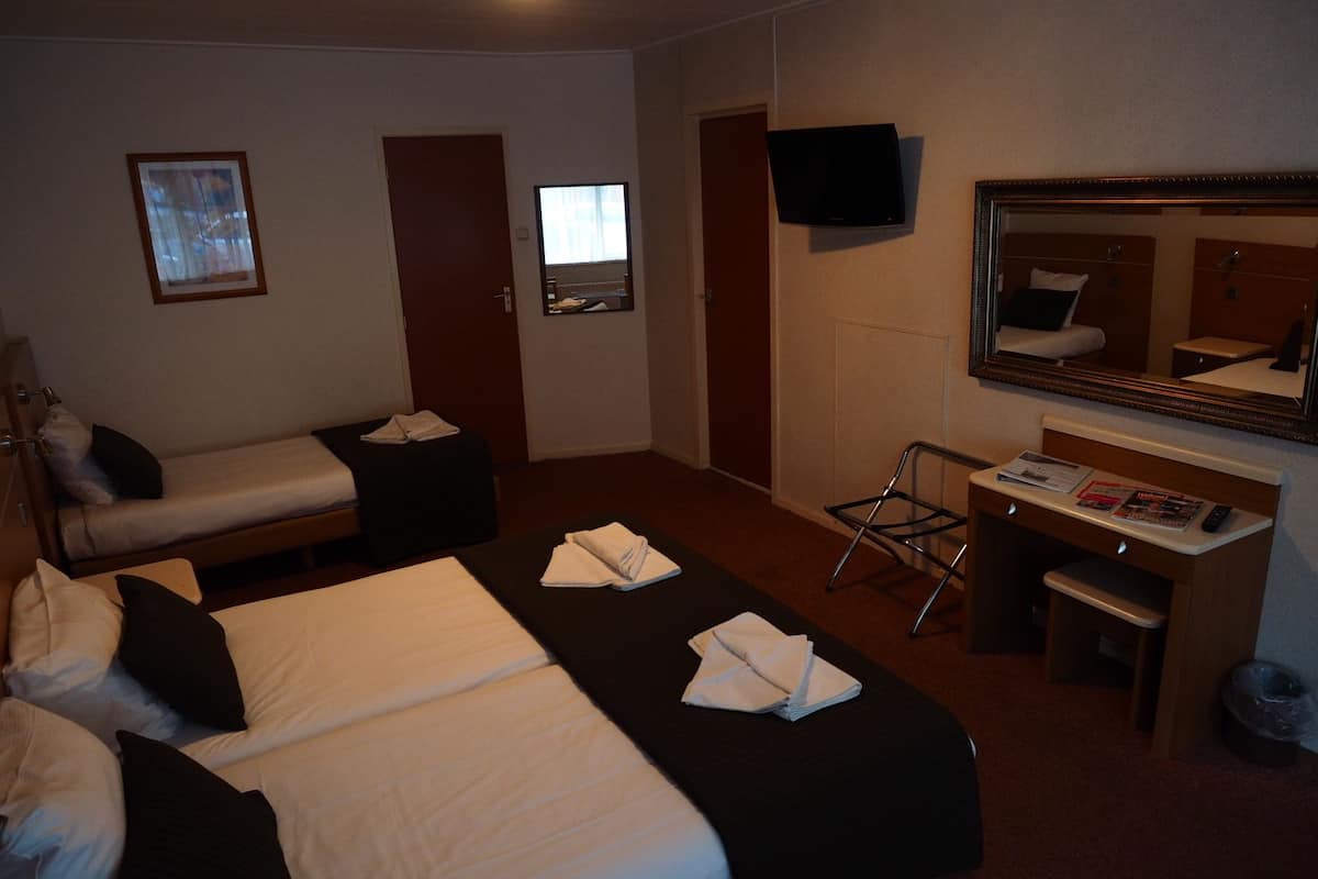A hotel room with two beds, a desk, a chair, a TV, a mirror, and a window.