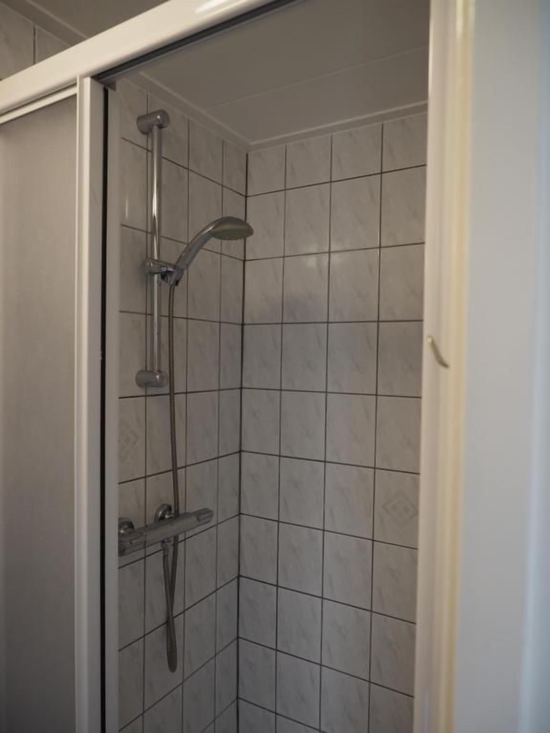 A shower with a handheld showerhead and a fixed overhead showerhead, enclosed by a glass door.