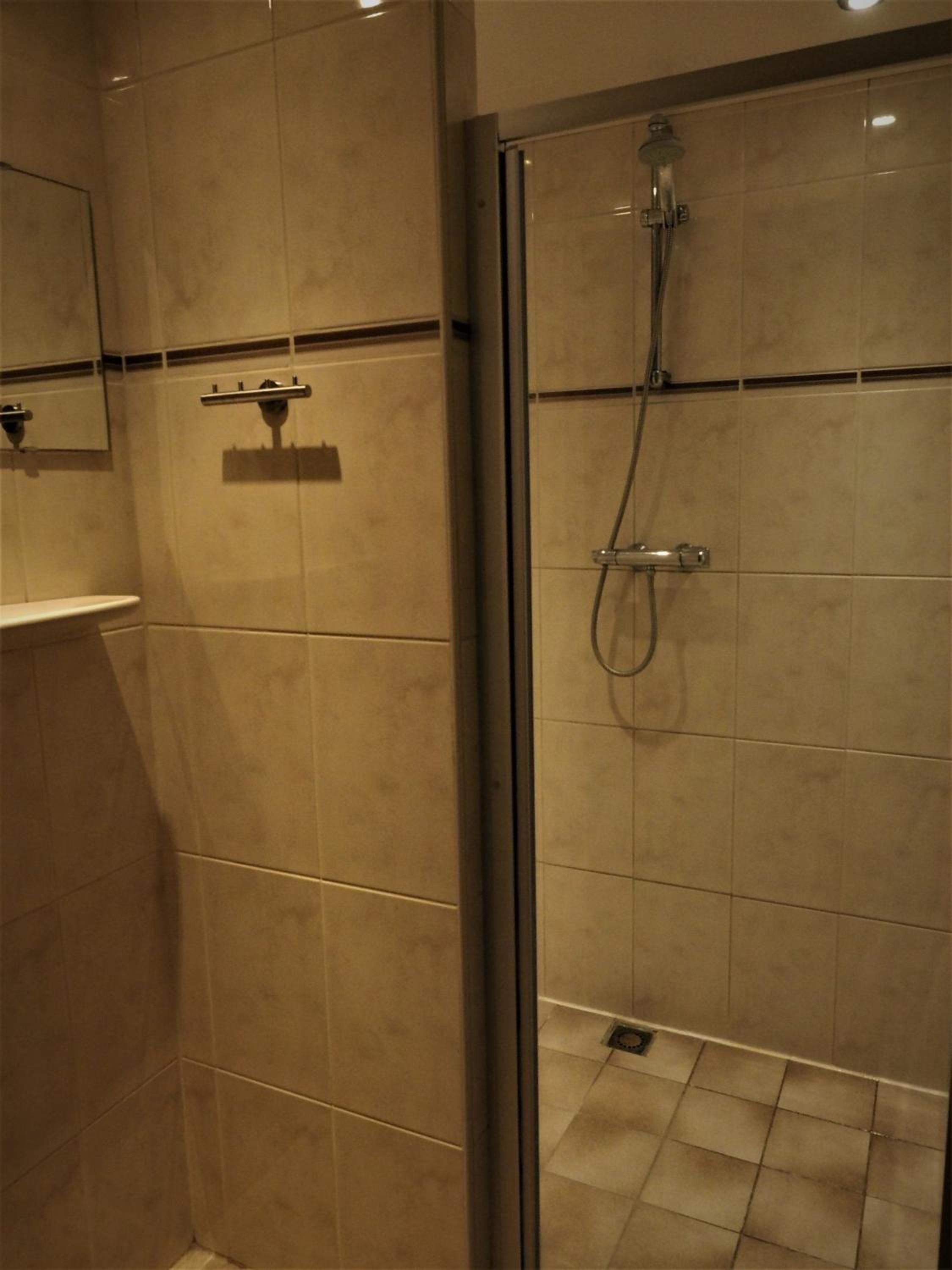Un baño con ducha envuelta en vidrio, un espejo y piso de azulejos.