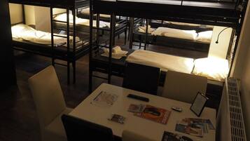 Un dormitorio con literas, una mesa con revistas y un ventanal con letrero de salida.