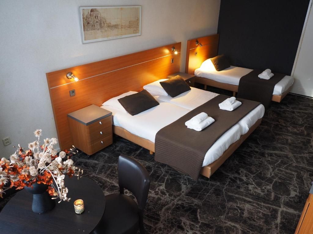 A hotel room with two beds, a small table with a vase, and a chair.