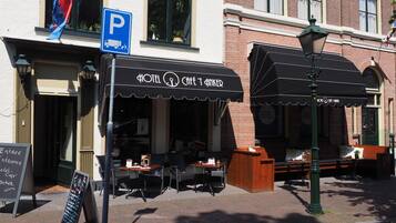 A hotel with outdoor seating, a blue parking sign, and a black awning.