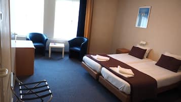 A hotel room with a bed, two chairs, a small table, a desk, and a radiator.