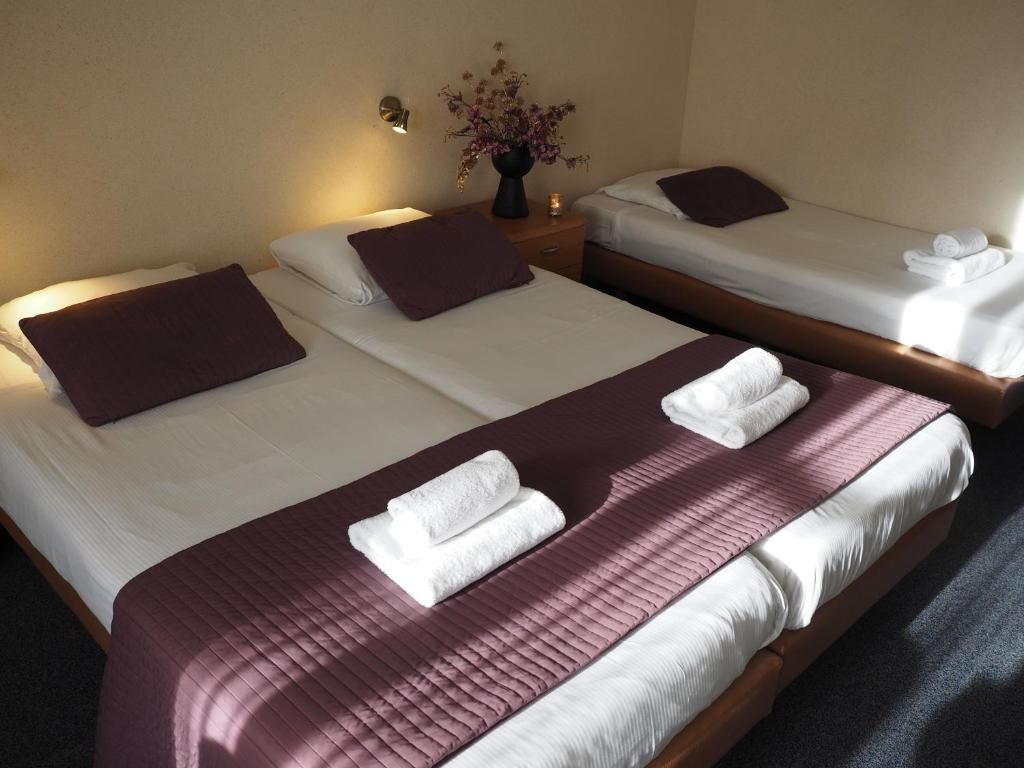 Habitación de hotel con dos camas, cada una con una almohada y una toalla doblada.