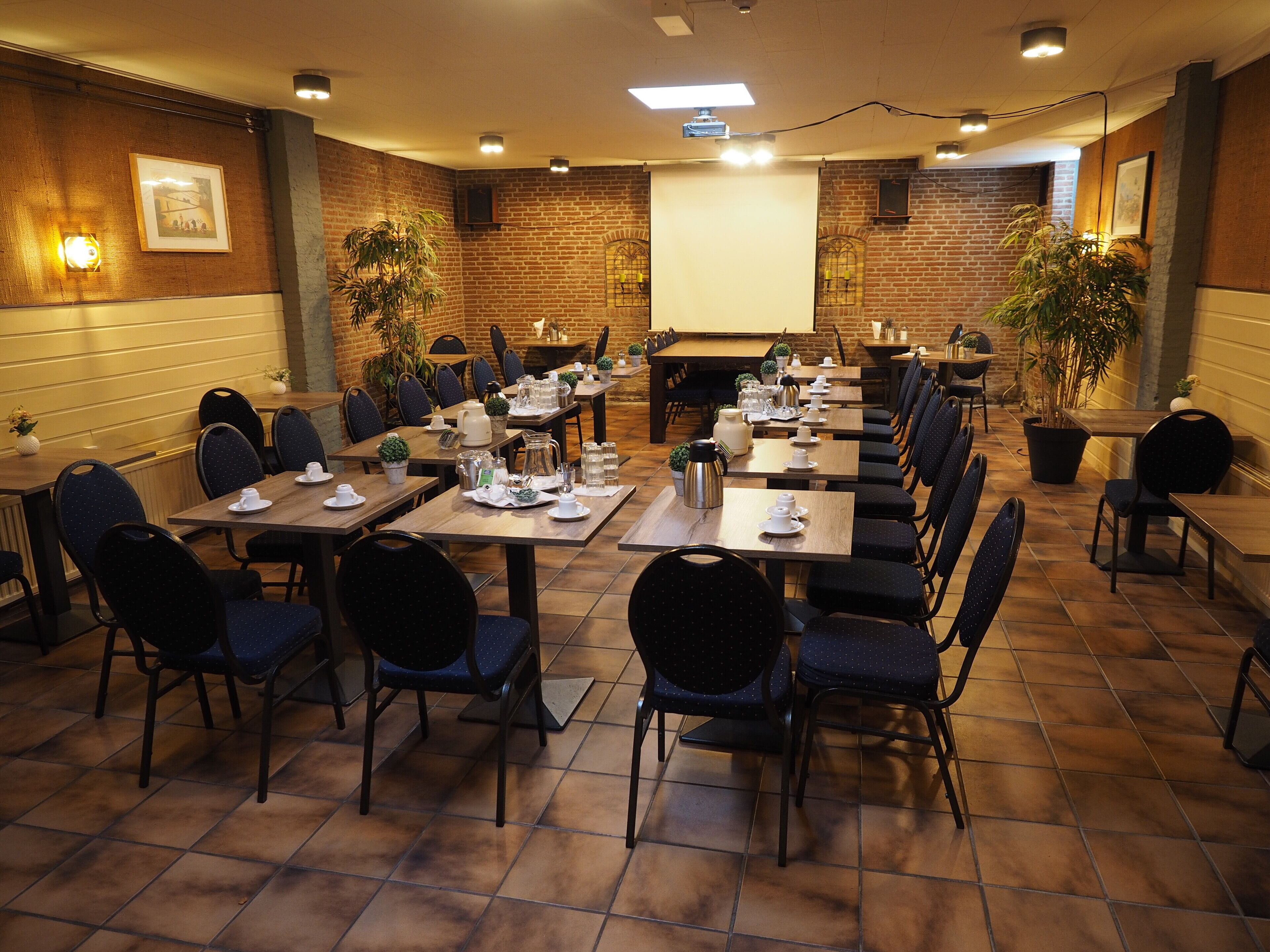 A conference room with multiple tables and chairs, equipped with presentation screens and lighting.