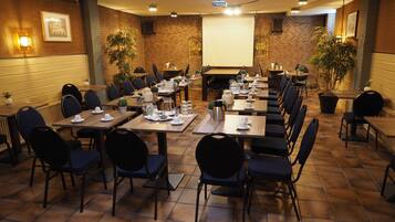 A conference room with multiple tables and chairs, equipped with presentation screens and lighting.