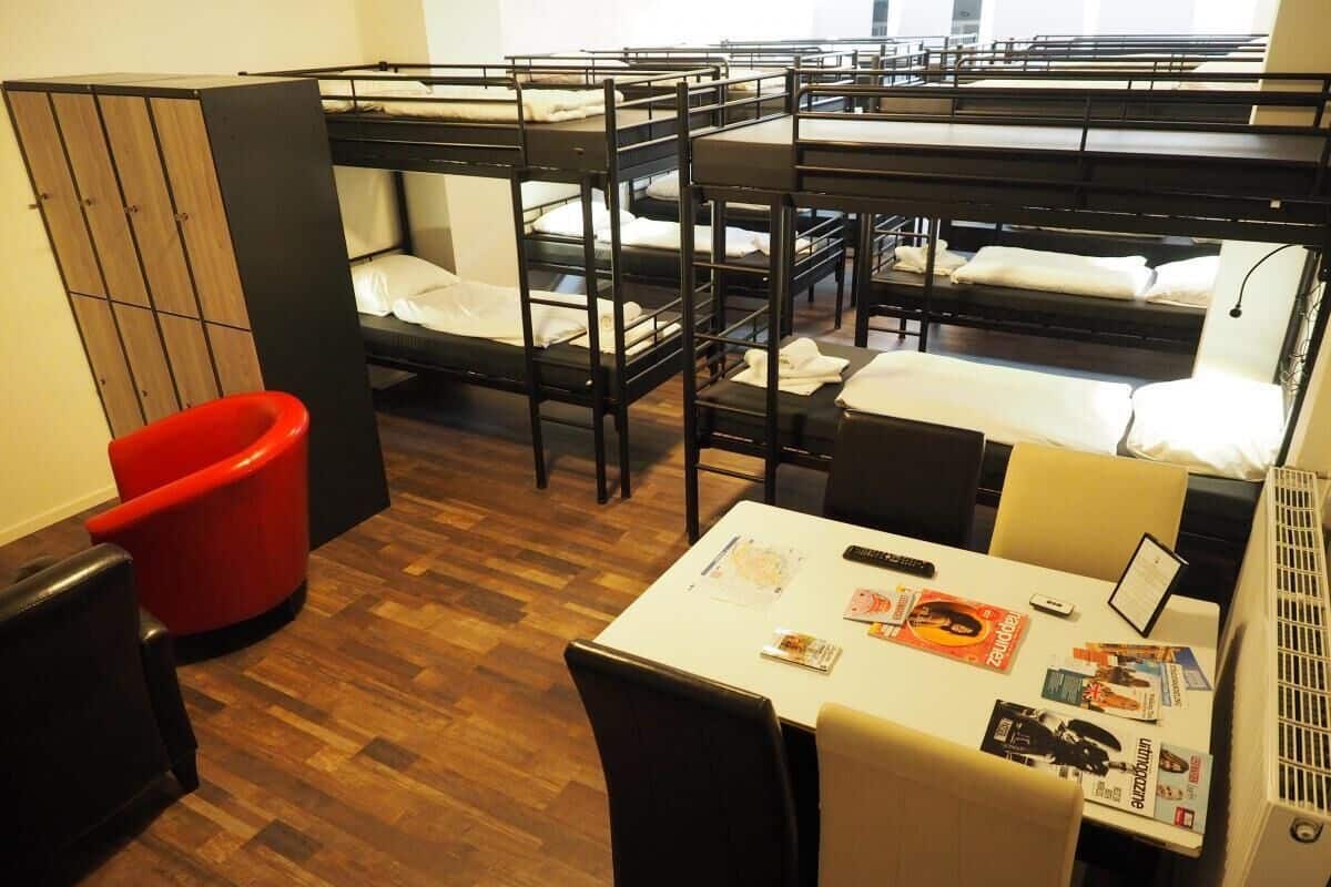 A dormitory room with bunk beds, a red chair, a table with magazines, and a radiator.