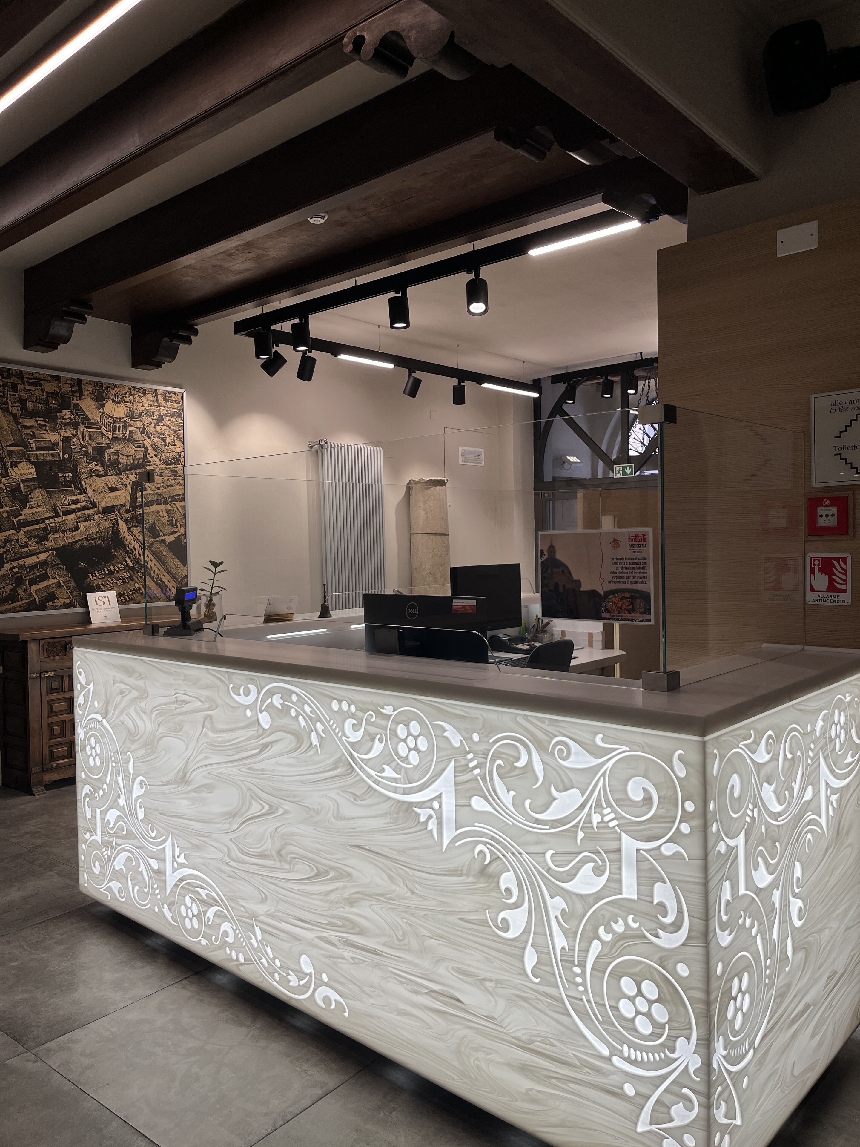 A reception desk with a marble design, overhead lighting, and a large wall mural.