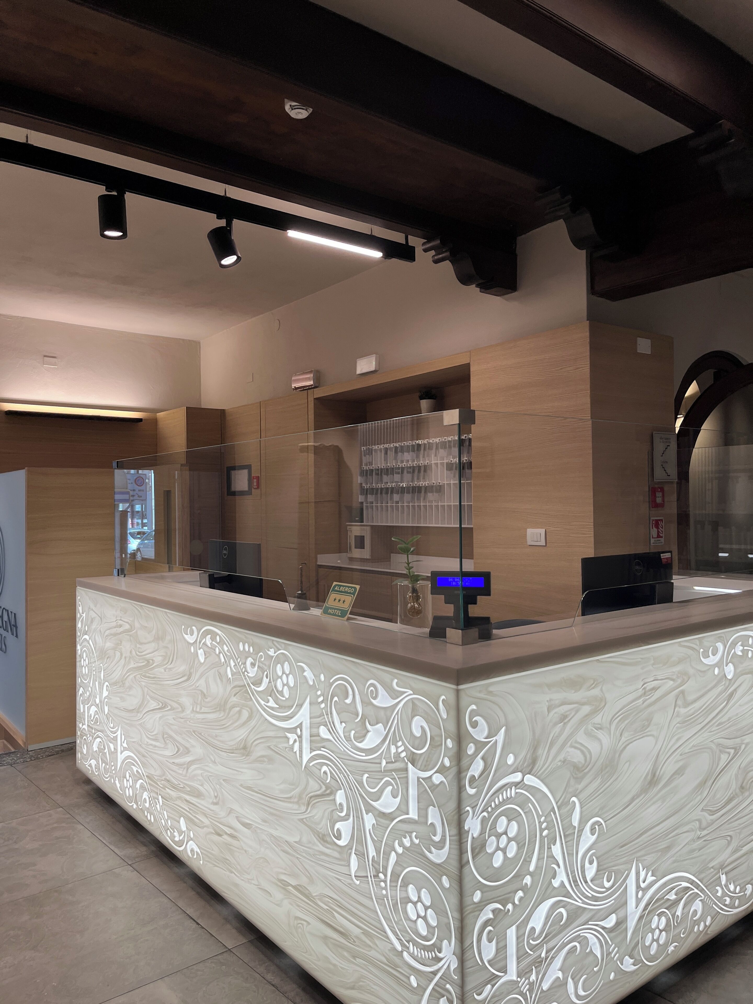 Una recepción de hotel con diseño de mármol, una pantalla digital y una partición de vidrio.