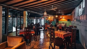 Un restaurante con mesas y sillas de madera, ventanas amplias y lámparas colgantes.