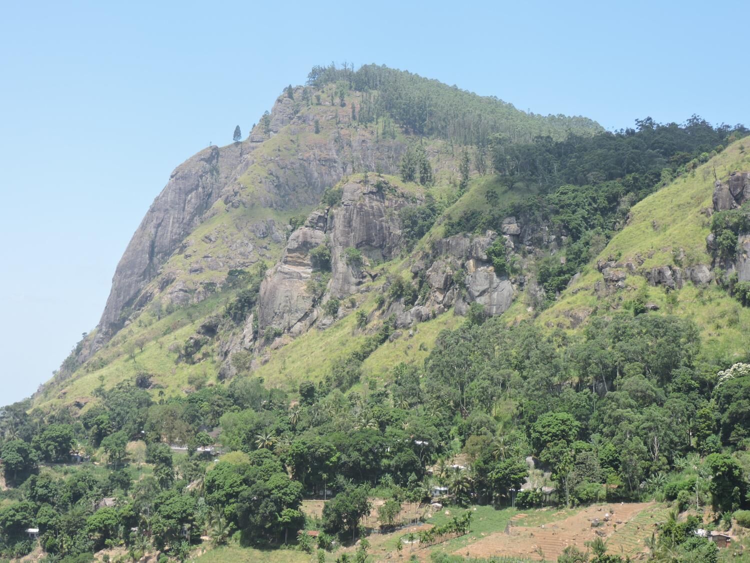 A mountainous landscape with a prominent rocky peak and dense greenery.