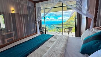 A bedroom with a bed, a view of the outdoors, and a table with chairs.