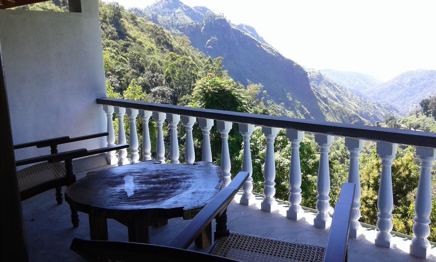 A balcony with a table and chairs, overlooking a mountainous landscape.