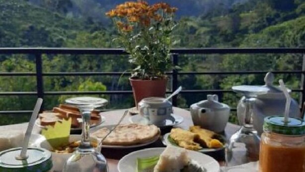 Una mesa con comida y bebidas en un balcón con vistas a colinas verdes.