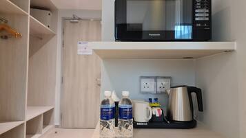 Un angolo cottura con un forno a microonde, due bottiglie d'acqua, una macchina da caffè e una tazza su uno scaffale.