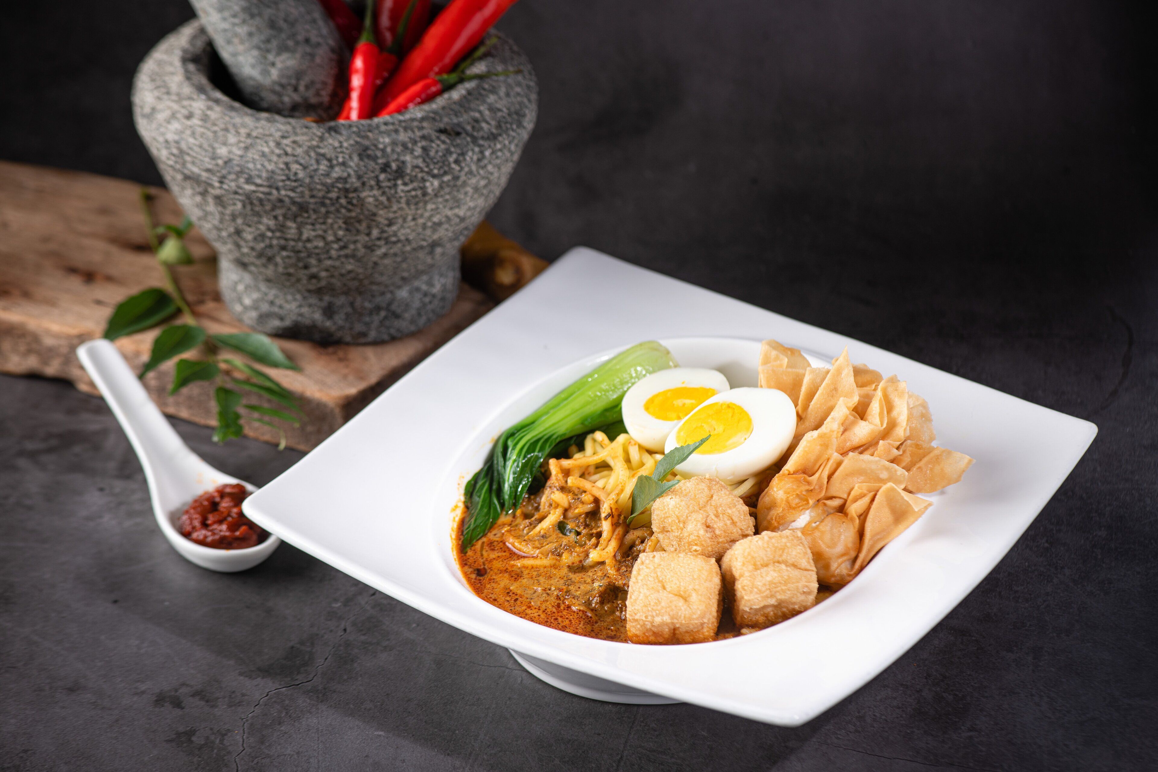 A square white plate with a noodle dish, egg, tofu, and vegetables.