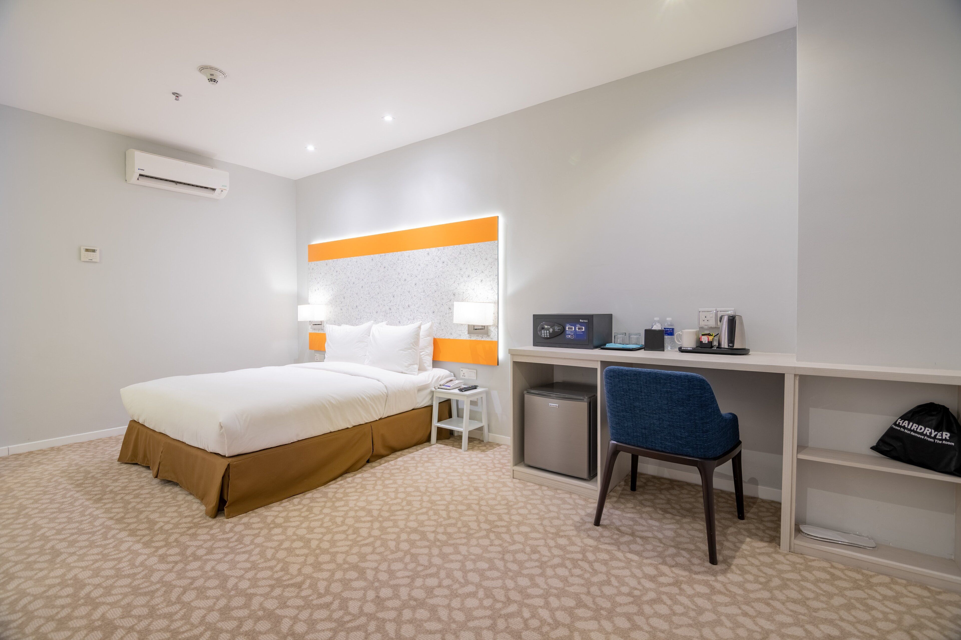 Una habitación de hotel con cama, escritorio, silla y un pequeño refrigerador.