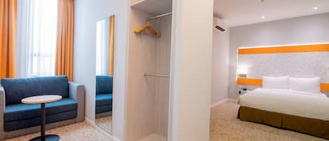 A hotel room with a bed, a sofa, a small table, and a walk-in closet.