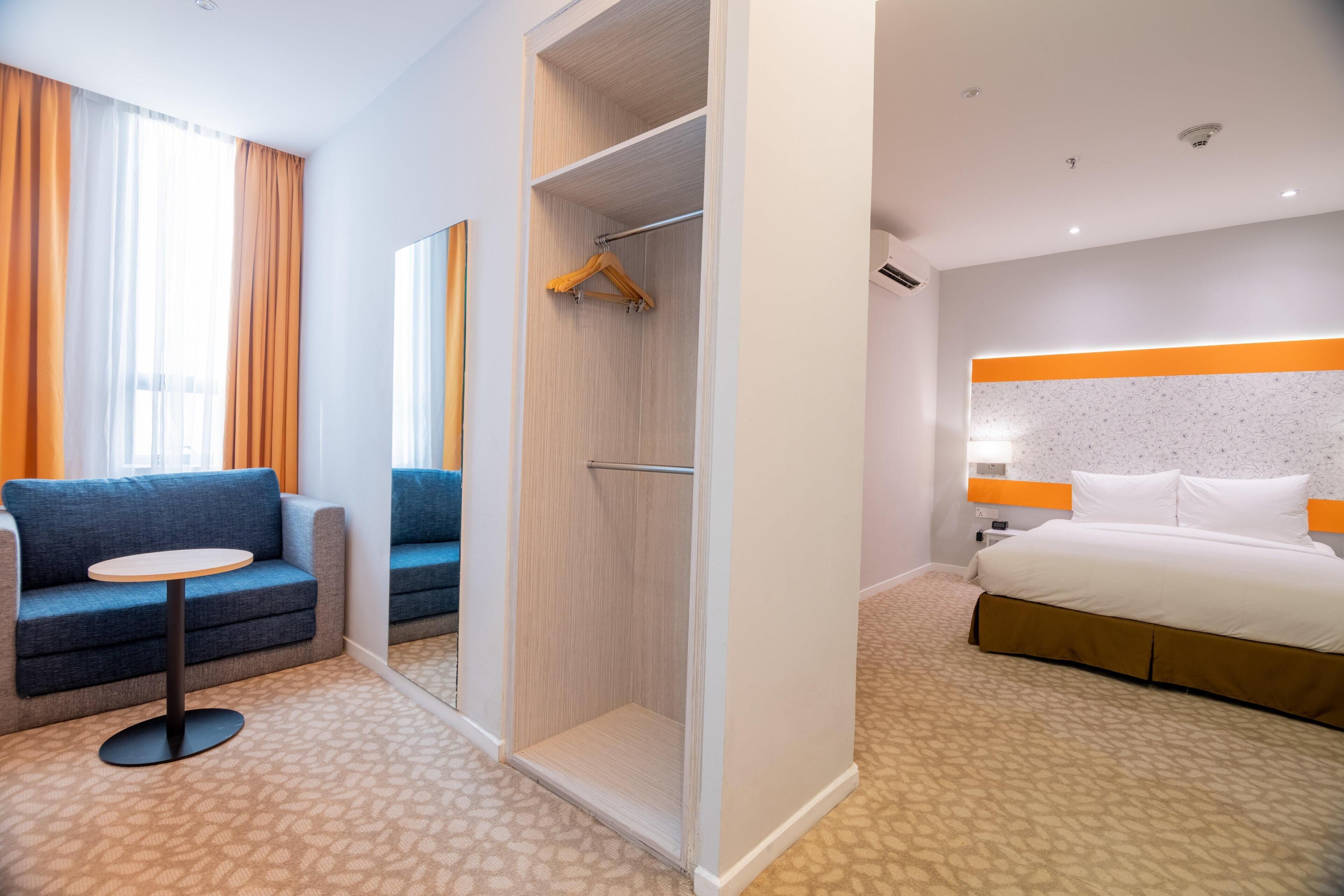 A hotel room with a bed, a sofa, a small table, a walk-in closet, and a mirror.