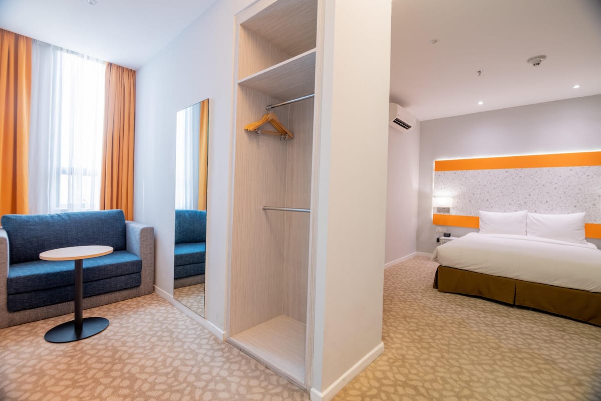 Quarto de hotel com cama, sofá, mesa pequena, closet espaçoso e espelho.