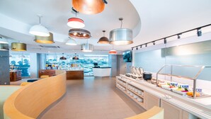 A modern cafe with a curved wooden bench, a buffet counter with various food items, and multiple pendant lights. - Holiday Inn Express & Suites Johor Bahru by IHG (Johor Bahru)