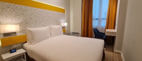 Habitación de hotel con cama, mesita de noche, lámpara y vistas al exterior a través de cortinas.