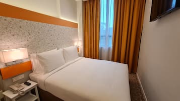 Ein Hotelzimmer mit einem Bett, einem Nachttisch mit Lampe, einem Telefon und einem an der Wand befestigten Fernseher.