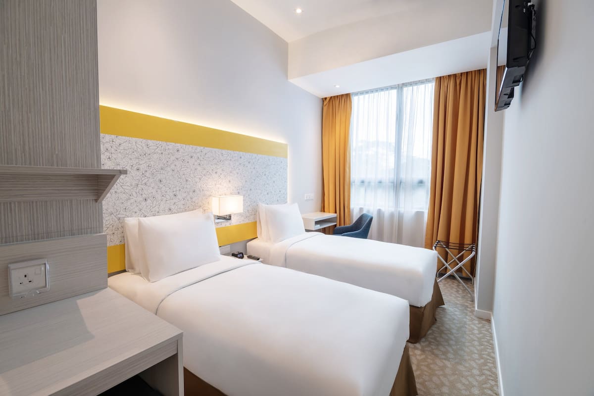 Ein Hotelzimmer mit zwei Betten, einem Schreibtisch, einem Stuhl und einem an der Wand befestigten Fernseher.