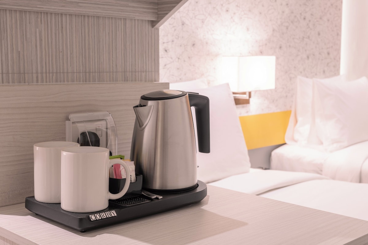 A hotel room with a coffee maker, two mugs, and a bed with white bedding.