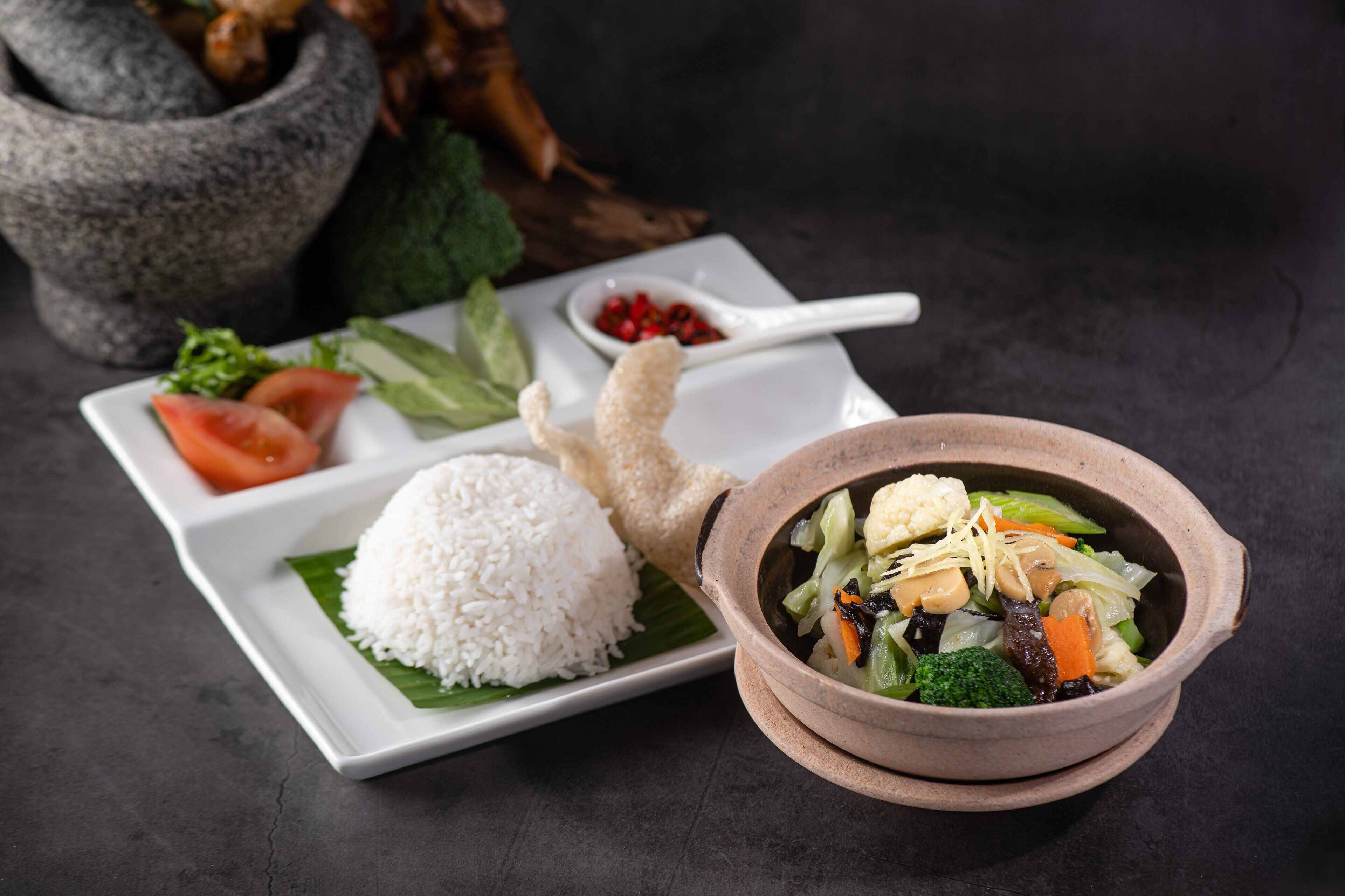 A plate with white rice, a bowl of vegetable soup, and a small dish of red chili peppers.