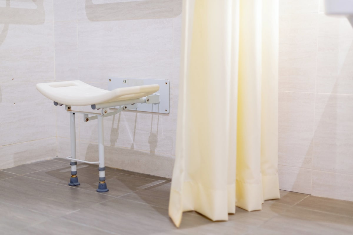 A white portable changing table with a footrest, mounted on a wall, and a yellow curtain partially drawn to the side.