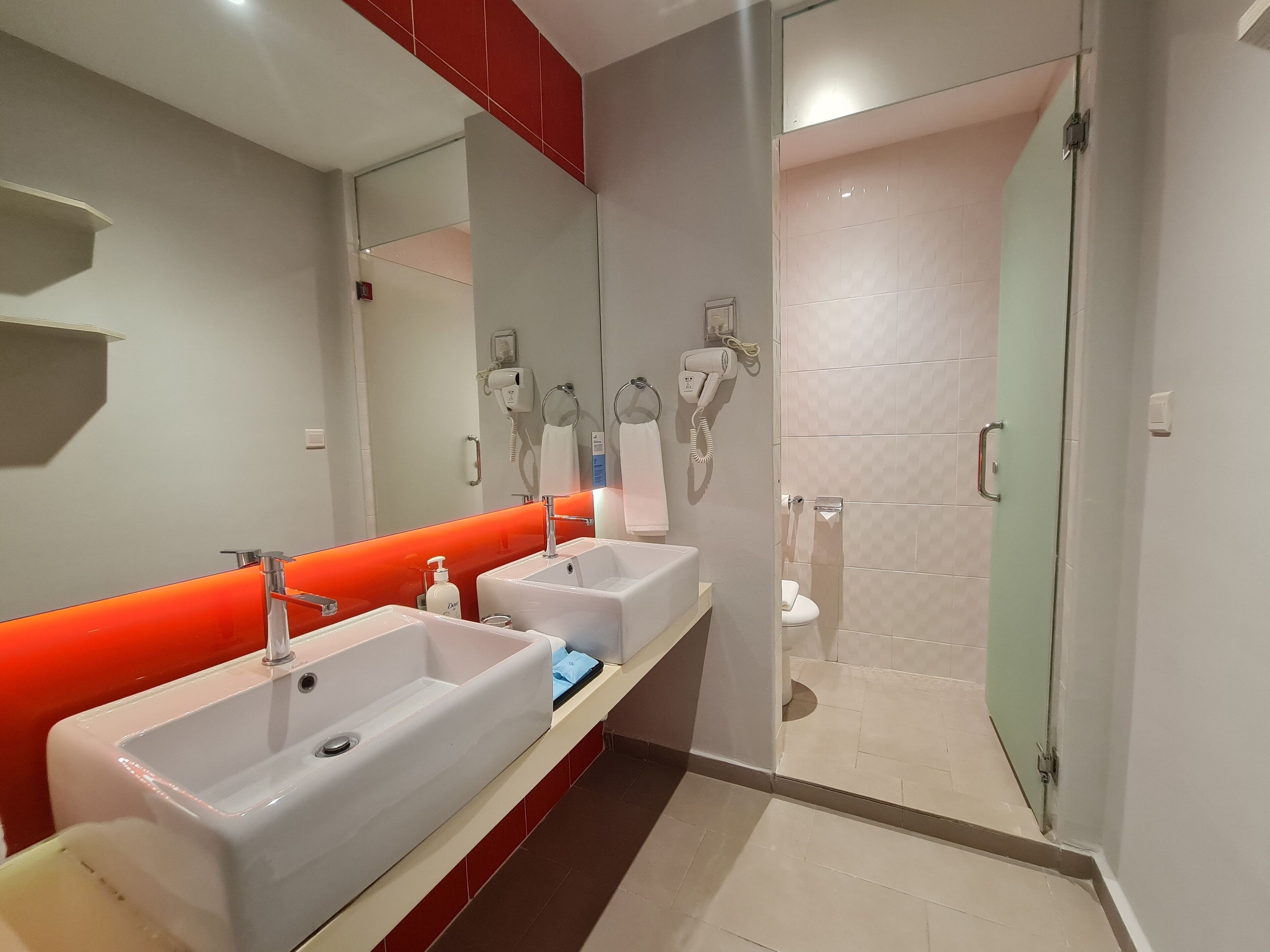 A modern bathroom with two sinks, a glass shower enclosure, and a red accent wall.