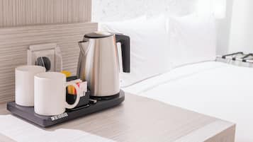 A hotel room with a bed, a bedside table with a coffee maker, two white mugs, and a tray with a bag of sugar and a spoon.