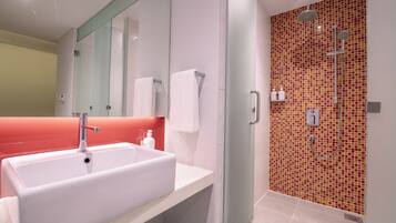 A modern bathroom with a large white sink, a glass shower enclosure, and a red-tiled shower wall.