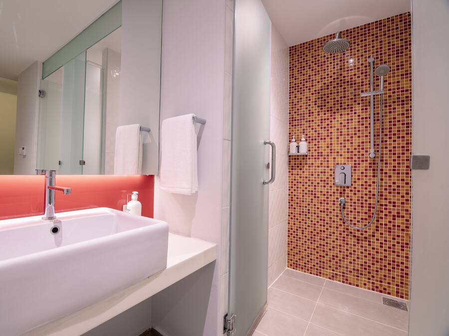 A modern bathroom with a large white sink, a glass shower enclosure, and a red-tiled shower wall.