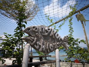Uma grande escultura de peixe de pedra, com a palavra "KONAK" escrita nela, rodeada por vegetação e um céu limpo.