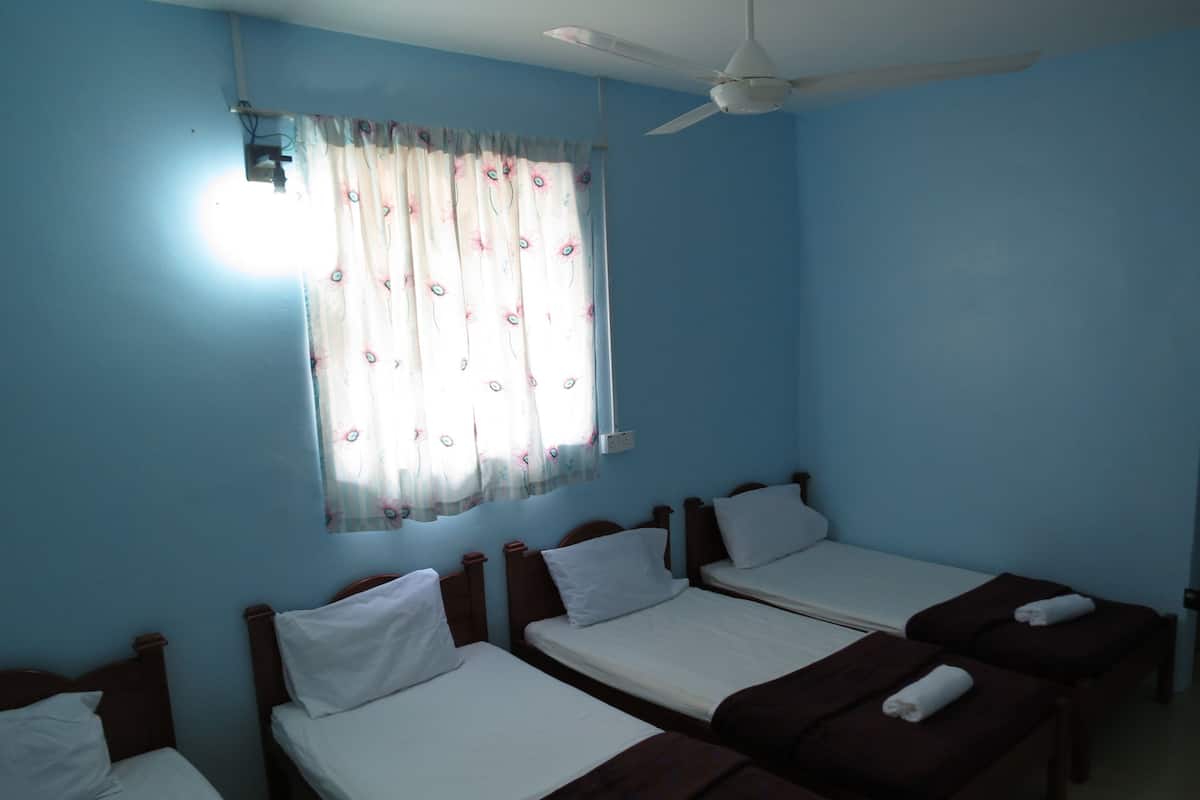 A room with four single beds, a ceiling fan, and a window with floral curtains.
