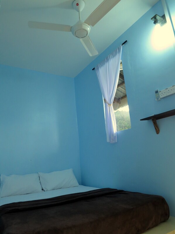 A room with a bed, a ceiling fan, a window with a curtain, and a wall-mounted electrical outlet.