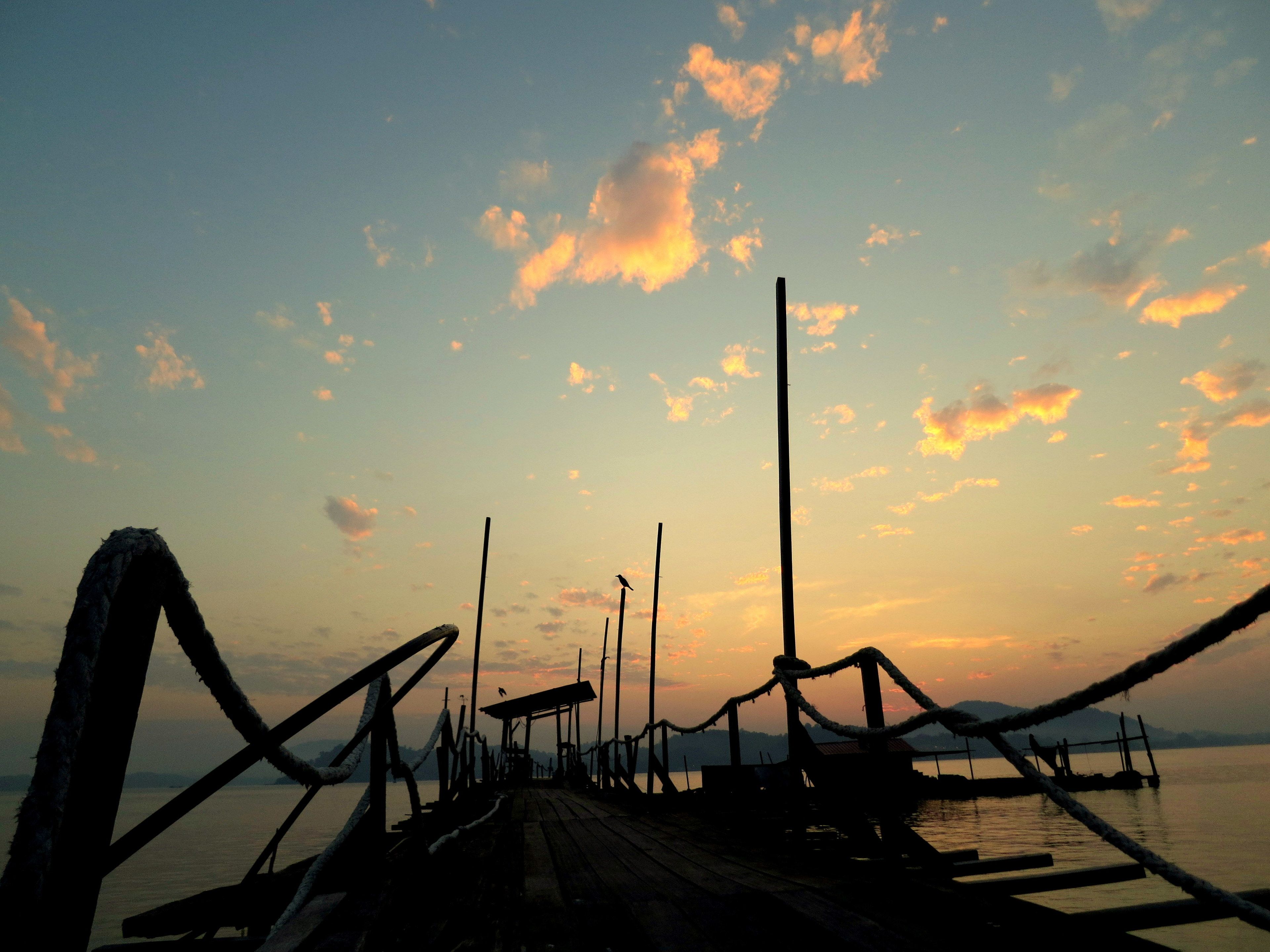 A wooden pier extending into calm water with a sunset in the background.