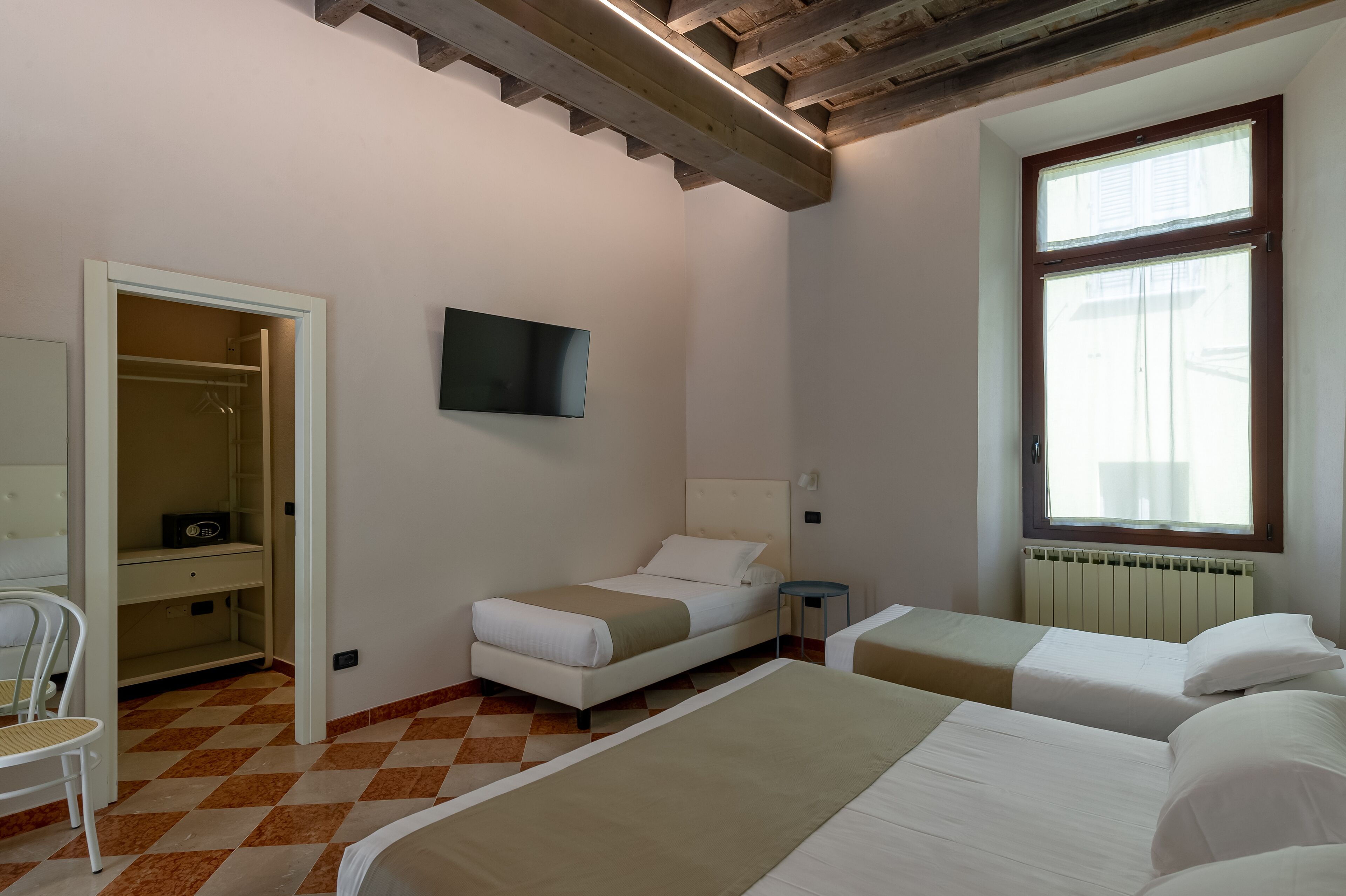 A hotel room with two beds, a wardrobe, a TV, and a window with blinds.