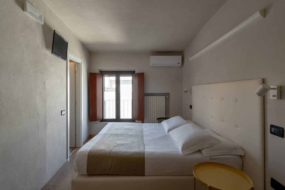 A hotel room with a bed, bedside table, and a window with blinds.