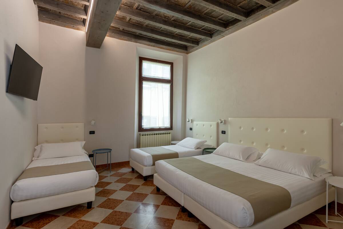 A hotel room with two beds, a window, a radiator, and a TV mounted on the wall.