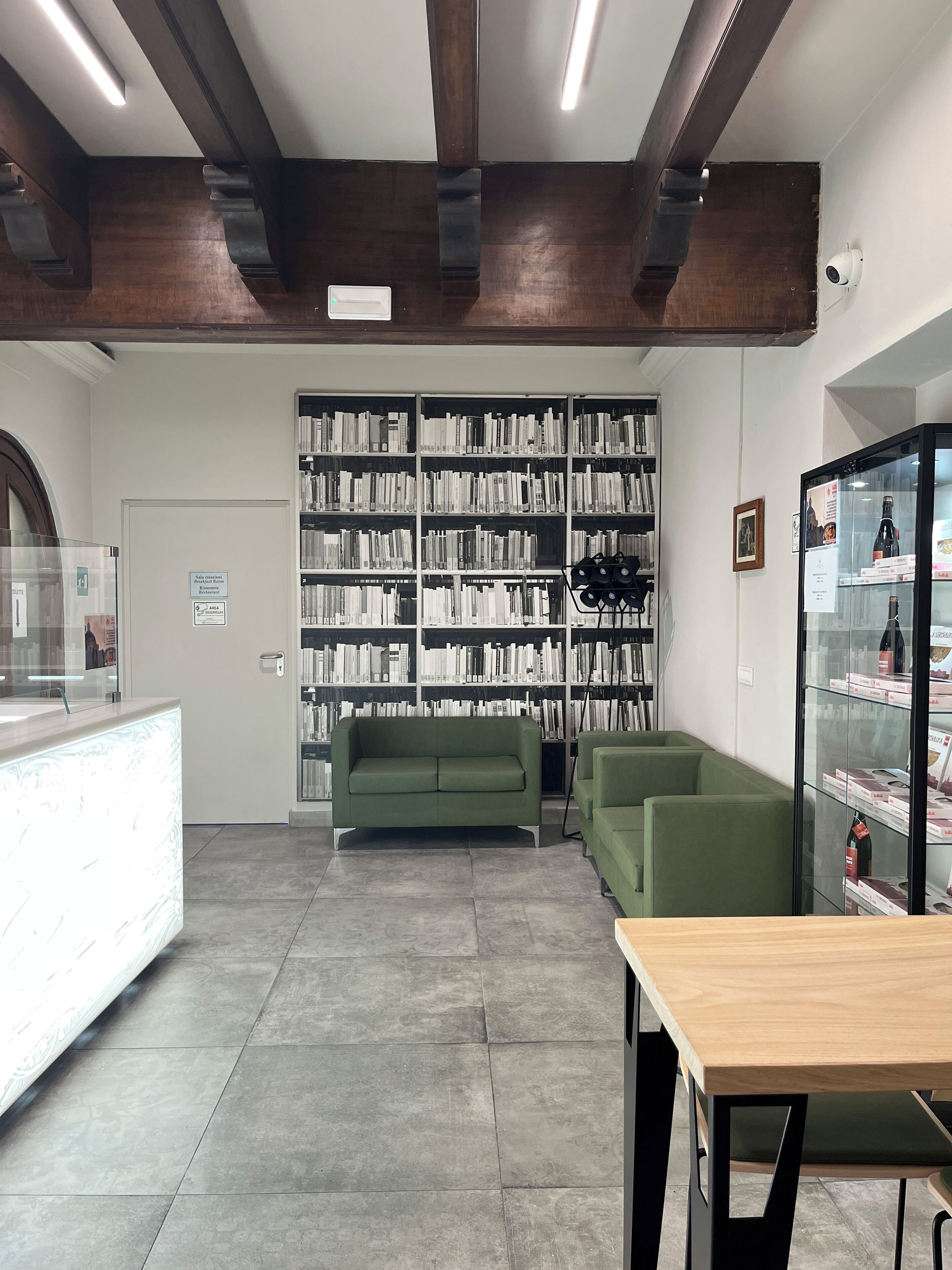 Una biblioteca con estanterías, un sofá verde, una vitrina de vidrio y una mesa de recepción.