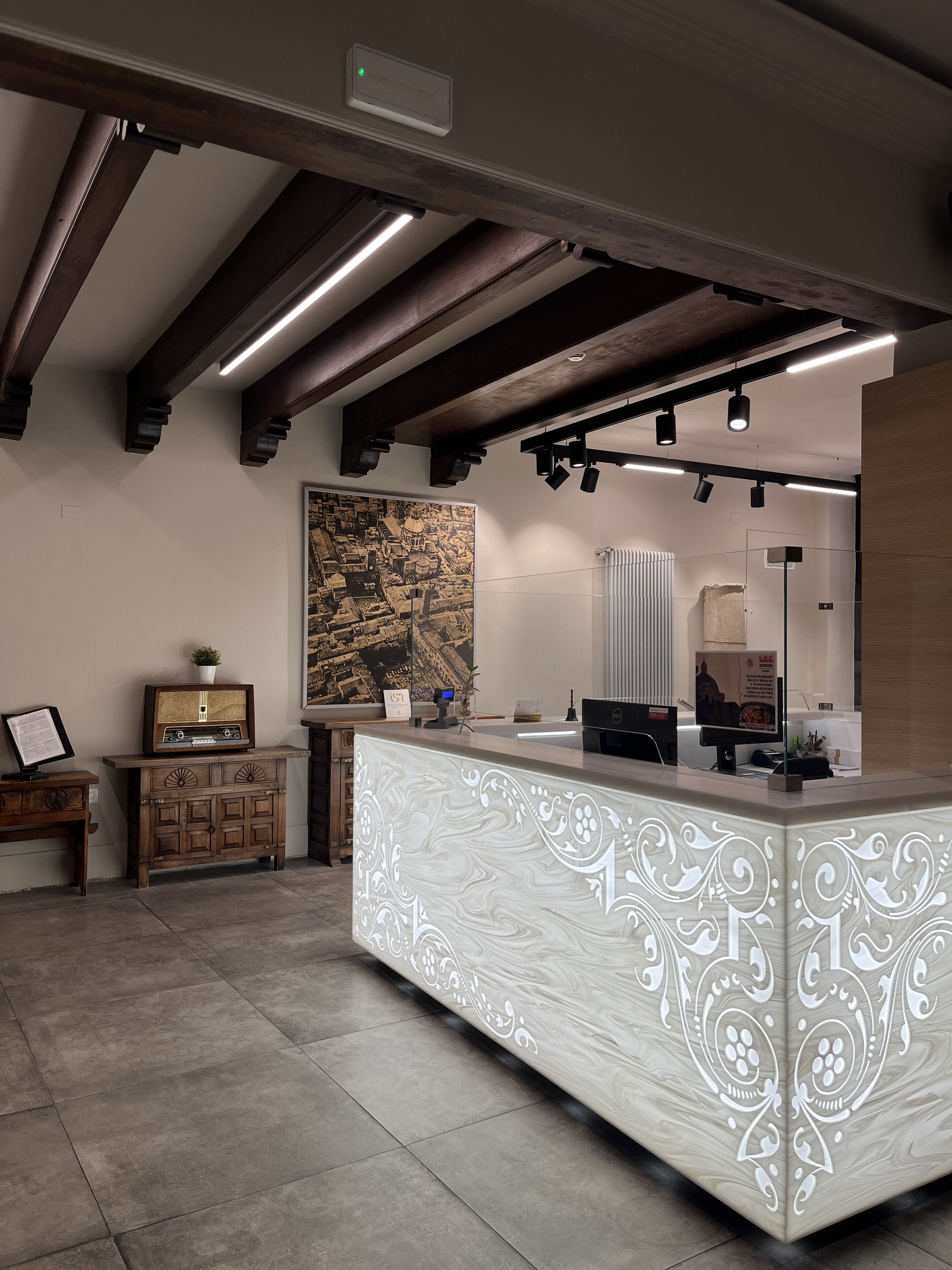 Un espace d’accueil doté d’un comptoir en marbre, de meubles en bois, d’un grand tableau représentant un paysage urbain et d’un éclairage moderne.
