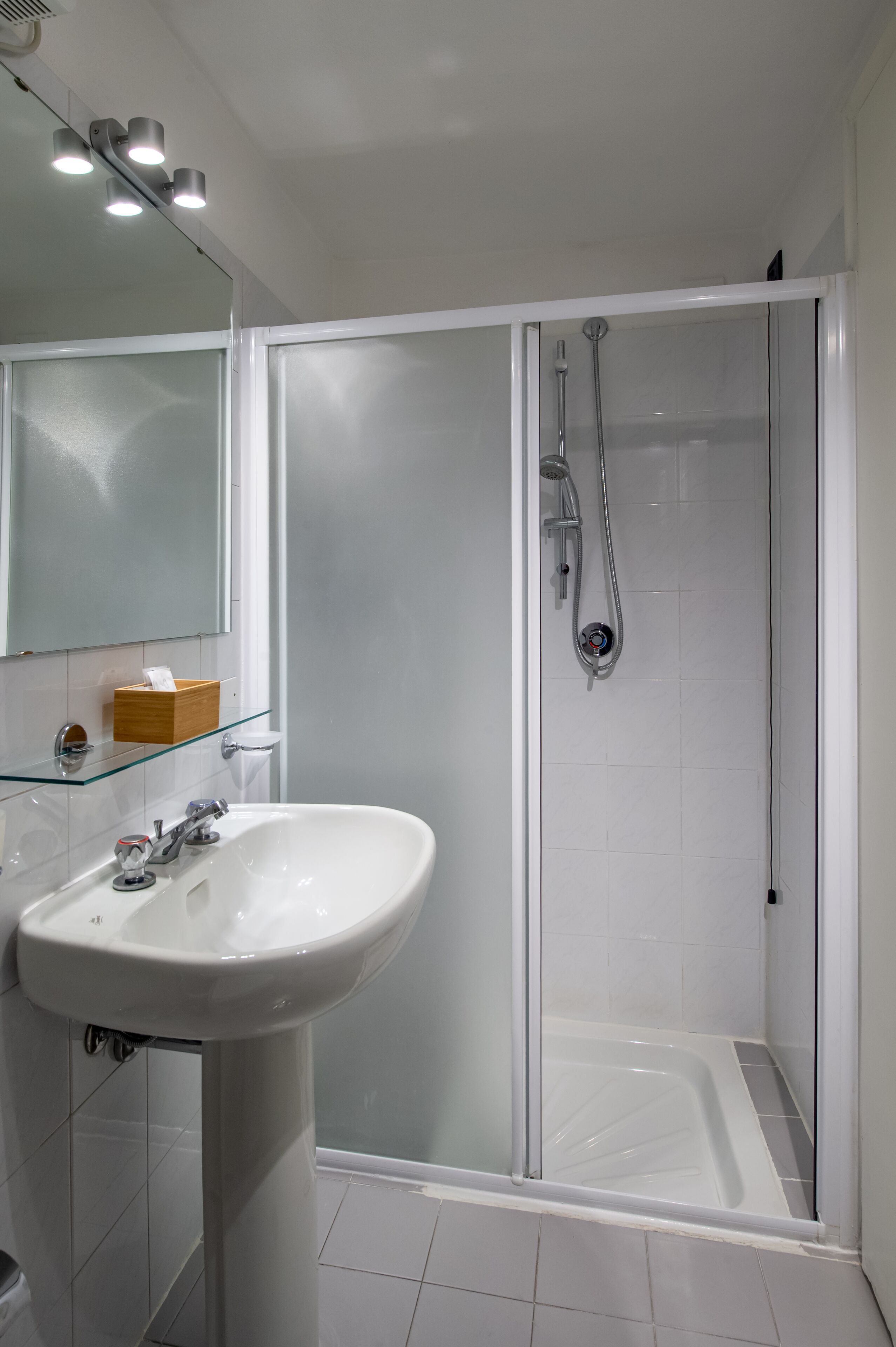 A modern bathroom with a glass shower enclosure, a white sink, and a mirror above the sink.