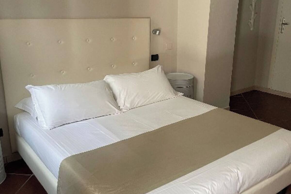 A neatly made bed with a headboard, a bedside table, and a wall-mounted light fixture.