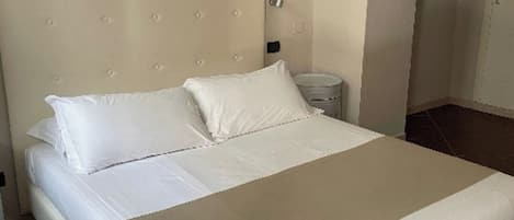 A neatly made bed with a headboard, a bedside table, and a wall-mounted light fixture.