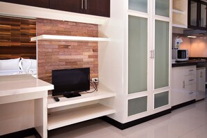 A modern kitchen with a flat-screen TV, white cabinets, and a brick accent wall. - Victorian Samui Condominium (Koh Samui)