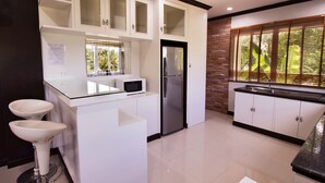A modern kitchen with white cabinetry, a stainless steel refrigerator, a microwave, and two sinks. - Victorian Samui Condominium (Koh Samui)