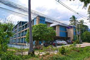 A multi-story hotel with balconies, parked vehicles, and surrounding greenery. - Victorian Samui Condominium (Koh Samui)